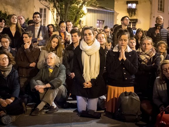 Menschen stehen, sitzen und knien zusammen, manche beten, am 15. April 2019 im Pariser Stadtteil Saint-Michel, während des Brandes der Kathedrale Notre-Dame.